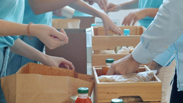 Close-up of hands putting groceries in containers collecting donation for charity in busy office. Teamwork and helping poor concept.