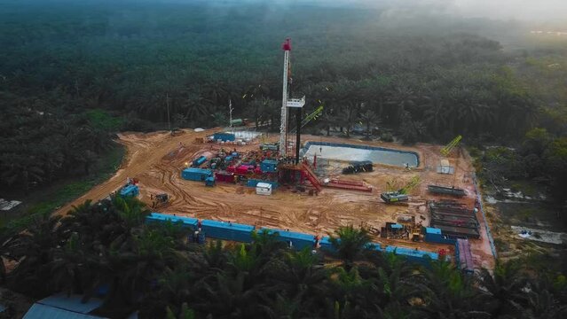 Cinematic Drone Shot of Onshore Drilling and Workover Rig structure and Rig equipment for oil exploration and exploitation in the middle of jungle surrounded by palm oil trees during sunset time.