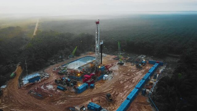 Cinematic Drone Shot of Onshore Drilling and Workover Rig structure and Rig equipment for oil exploration and exploitation in the middle of jungle surrounded by palm oil trees during sunset time.