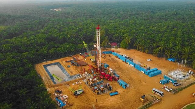 Cinematic Drone Shot of Onshore Drilling and Workover Rig structure and Rig equipment for oil exploration and exploitation in the middle of jungle surrounded by palm oil trees during sunset time.