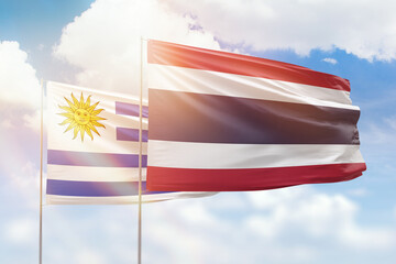Sunny blue sky and flags of thailand and uruguay