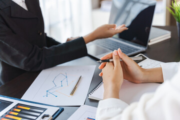Two pretty young Asian businesswoman sitting at desk with laptop doing paperwork together discussing project financial report. Corporate business collaboration concept.