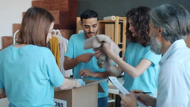 Diverse group of people volunteers packing boxes with clothing for donation working in charity organization together. Activism and helping poor concept.
