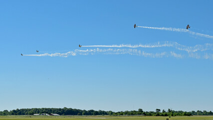 Stunt biplanes, trailing smoke behind them begin to roll out of formation.