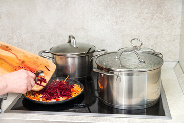Close-up of a woman's hand mixing beetroot sliced on a wooden board, carrots, garlic in a frying pan