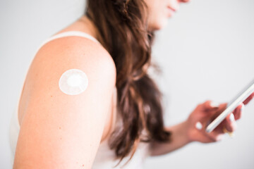 woman showing covid-19 or flu vaccination band-aid on her arm while looking at her phone,...