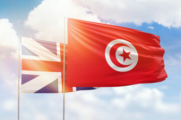 Sunny blue sky and flags of tunisia and great britain