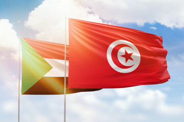 Sunny blue sky and flags of tunisia and sudan