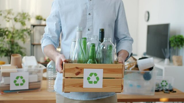 Close-up of male hands holding wooden box with glass bottles for recycling standing at home alone. Zero waste and environment concept.