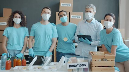 Portrait of volunteers in medical masks providing food for hungry people standing in charity fund office. Humanitarian crisis and solidarity concept.