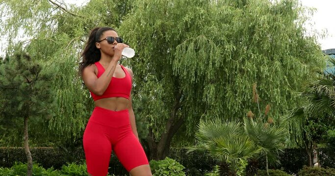 Woman drinking water from bottle after gym after working out, outdoor sport black girl drink clear mineral water after training.