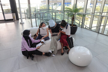 Four young attractive Asian group woman friends colleagues students indoor building sit on modern bench talk discuss study research mingle relax