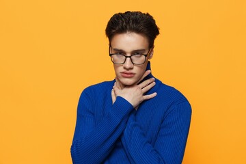 Fototapeta premium a handsome man stands in black glasses for vision in a blue zip-up jacket, posing on an orange background with his hand on his neck