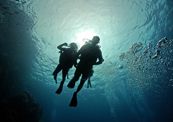 Two scuba divers close to ocean surface looking down in silhouette withe sun behind them - Sail...