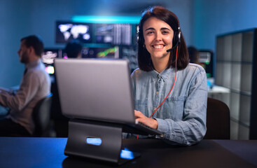 Smiling young female caucasian financial analyst working in the office with laptop and headset looking at camera.