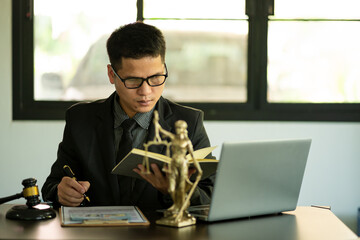 Middle aged Asian male lawyer working on laptop and legal contract documents in courtroom Judge's...