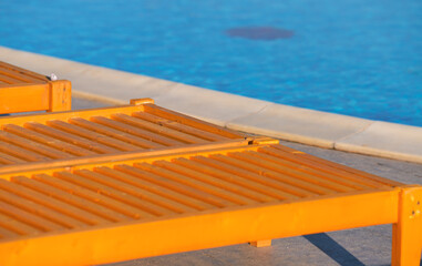 Detail view of some wood sun-beds next to a blue water swimming pool