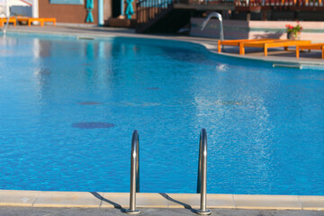 The ladder of a luxury swimming pool with crystal clear blue water. Summer vacation and relaxation spot.