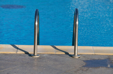 The ladder of a luxury swimming pool with crystal clear blue water. Summer vacation and relaxation spot.