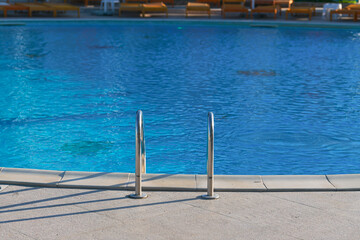 Fototapeta na wymiar The ladder of a luxury swimming pool with crystal clear blue water. Summer vacation and relaxation spot.