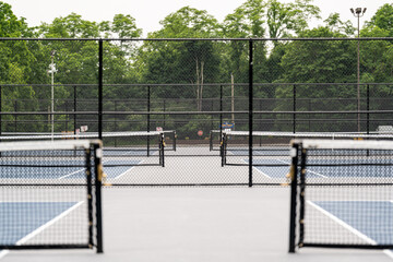 Tennis court net posts, looking between several tennis courts, blue tennis court with white lines and gray out of bounds	