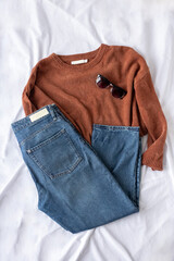 Clothing women flat lay with blue jeans, brown sweater, black sunglasses on white