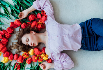A young woman is lying on the floor among red tulips. The concept of March 8, Valentine's Day. Spring portrait of a woman.