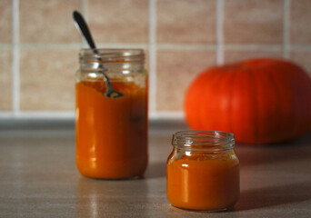 baby pumpkin puree in a glass jar with a spoon and fresh pumpkin