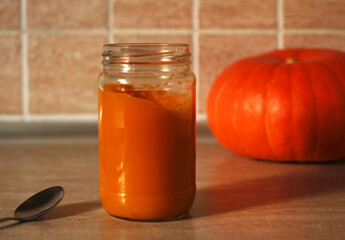 baby pumpkin puree in a glass jar with a spoon and fresh pumpkin