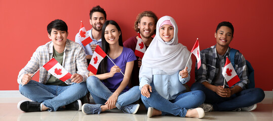 Group of students with Canadian flags sitting near red wall - obrazy, fototapety, plakaty