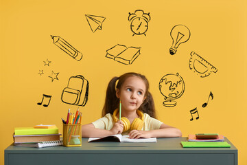 Thoughtful little schoolgirl sitting at desk against yellow background