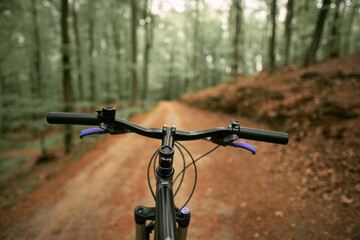 Naklejka na ściany i meble Mountain bike handlebar viewed from the first-person perspective. visible bicycle frame and bicycle accessories on the handlebar and the forest trai. Concept of spending time outdoors while bikeriding