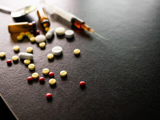 Narcotics concept. Ecstasy Pills and syringe on black wooden table background. card and poster for...