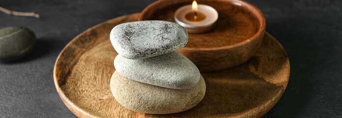 Wooden tray with stack of stones and candle on dark background. Zen concept