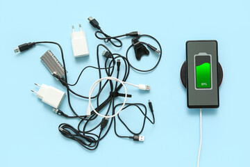 Modern mobile phone charging with wireless pad and different cables on color background