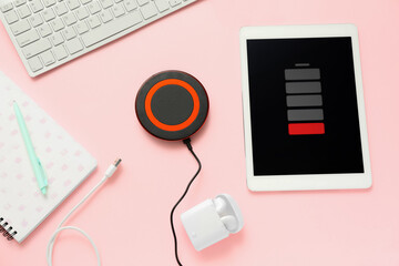 Wireless charger pad, uncharged tablet computer and stationery supplies on color background