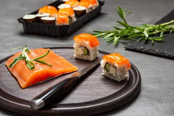 Salmon, knife and salmon sushi on cutting board.