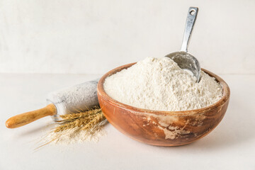Bowl with wheat flour and rolling pin on light background