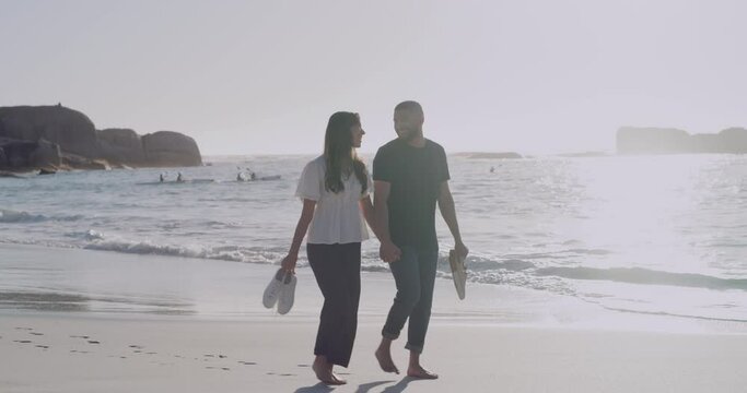 Happy And Loving Couple Enjoying A Romantic Walk At The Beach Together. Cheerful Affectionate Boyfriend And Girlfriend Holding Hands While Bonding On Honeymoon Vacation, On The Beach At Sunset