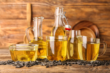 Glass containers of oil with sunflower seeds on wooden background