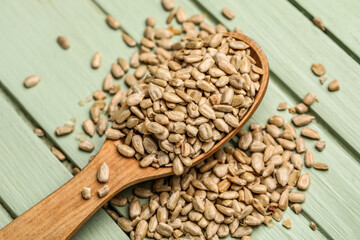 Spoon with peeled sunflower seeds on green wooden background, closeup
