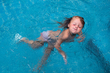 A little girl with blue eyes is bathing in the blue water of the pool. Summer children's games....