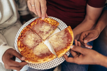 Hands taking pizza slices from plate, close up view
