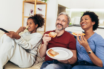 Portrait of happy family sharing pizza at home and watching tv.