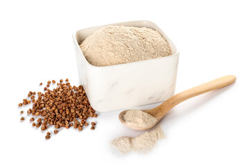 Bowl of flour, spoon and buckwheat grains on white background