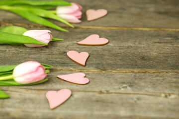 Bright pink tulips and hearts on the surface of a wooden table. Copy space.