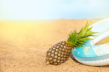 Pineapple with a swimming circle lying on the sand of the beach against the background of the sea