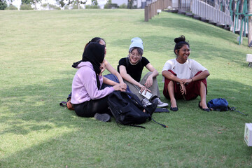 Four young attractive Asian group woman friends colleagues students outdoor green grass field sit on ground talk discuss enjoy backpack copy book cellophane