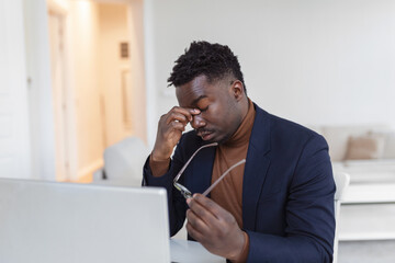 Stressed tired African American man touching temples, suffering from headache after long hours...