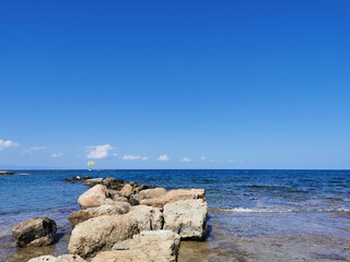 Coast of the Mediterranean Sea, waves, clear water, stone ridge against the blue sky with clouds boat with a yellow parachute.